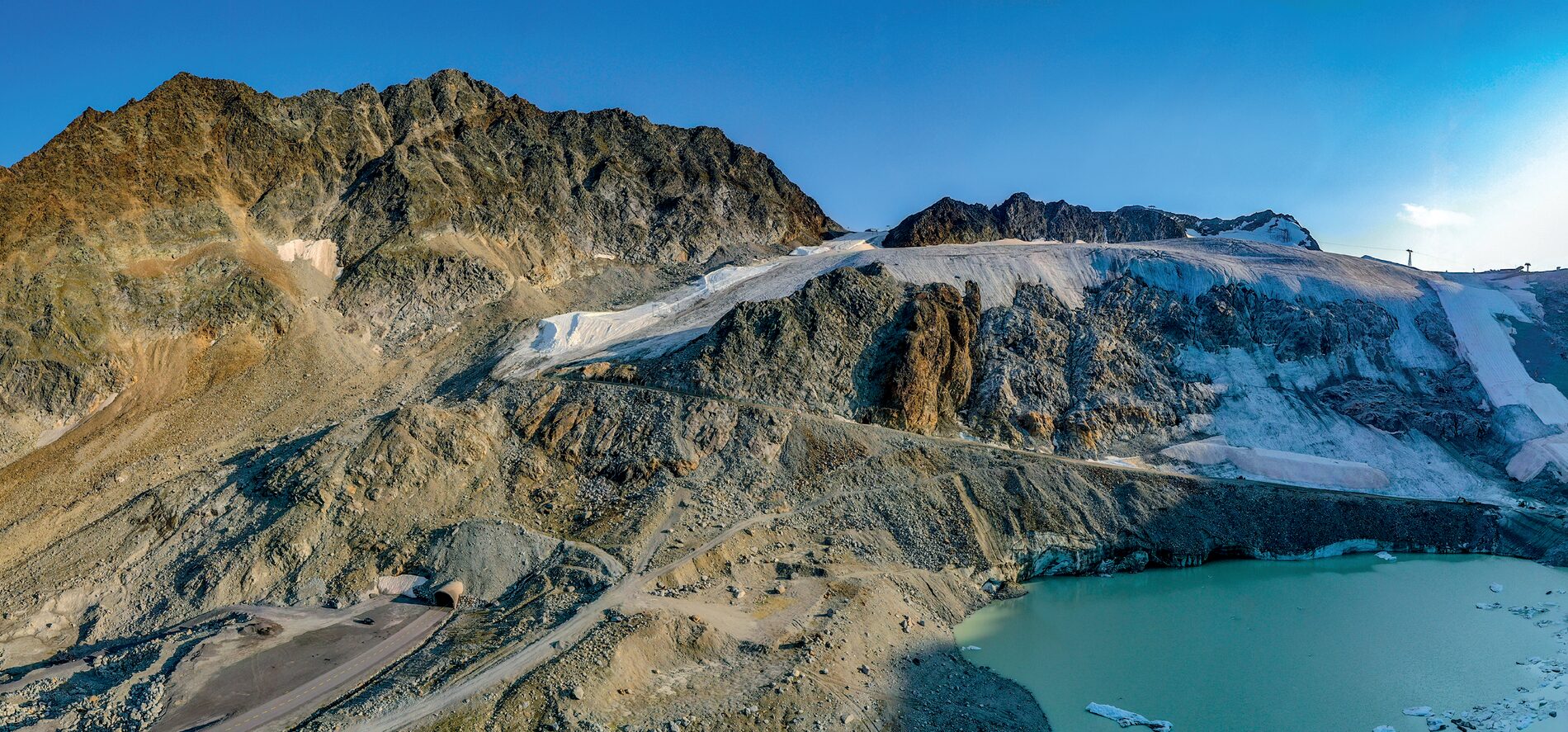 Gletscher über einem türkisfarbenen Schmelzwassersee, links ein Tunnelportal in einer Geröllhalde Gletscher über einem türkisfarbenen Schmelzwassersee, links ein Tunnelportal in einer Geröllhalde