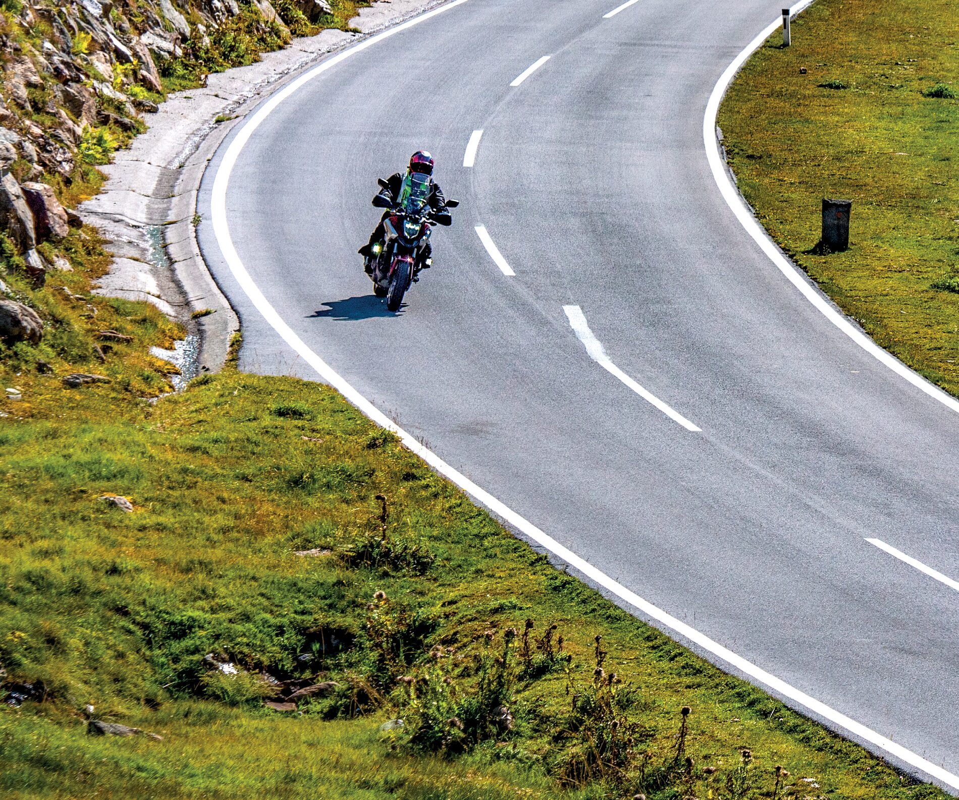Motorradfahrer in einer weiten Kurve zwischen Grashang und Steinmauer Motorradfahrer in einer weiten Kurve zwischen Grashang und Steinmauer