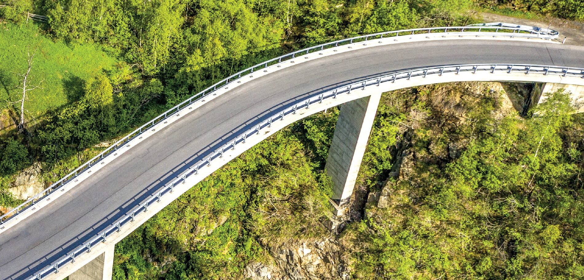 Luftbild einer geschwungenen Straßenbrücke auf Betonpfeilern über einer bewaldeten Schlucht Luftbild einer geschwungenen Straßenbrücke auf Betonpfeilern über einer bewaldeten Schlucht